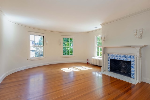 unfurnished living room featuring a tile fireplace, radiator heating unit, light hardwood / wood-style floors, and plenty of natural light