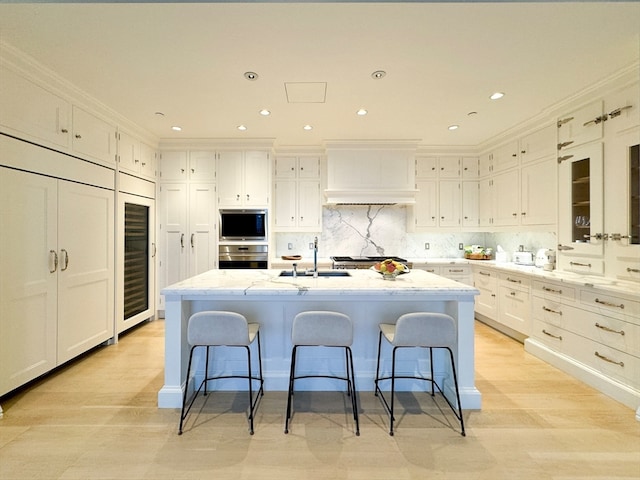 kitchen featuring white cabinetry, a breakfast bar area, a center island with sink, and stainless steel oven