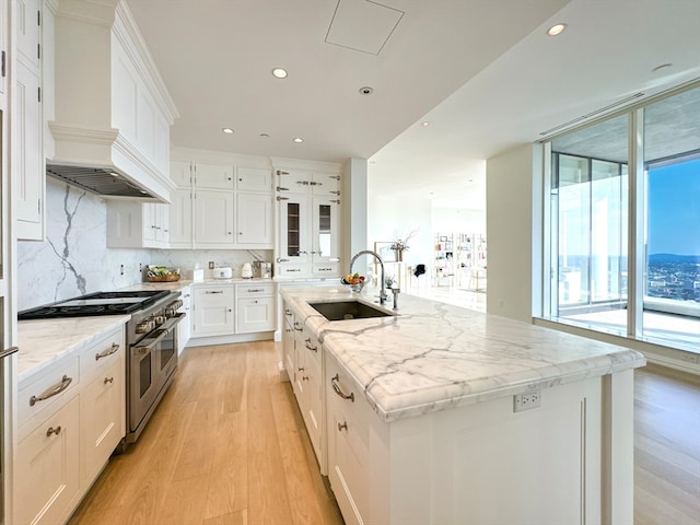 kitchen with light stone countertops, light hardwood / wood-style floors, sink, a kitchen island with sink, and double oven range