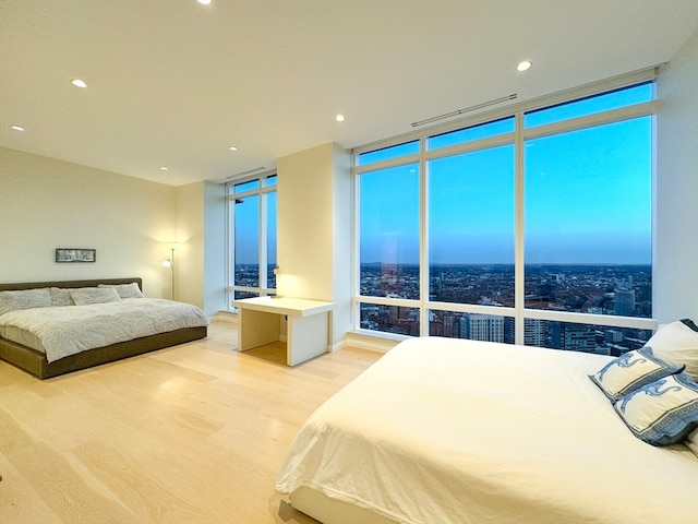 bedroom with light wood-type flooring, a wall of windows, and multiple windows