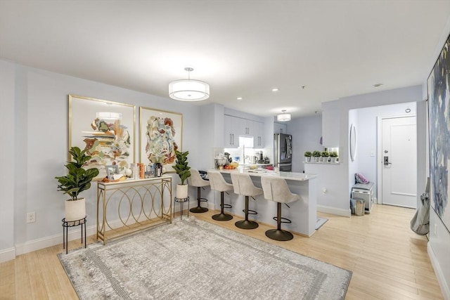 kitchen with light countertops, a peninsula, a kitchen bar, light wood-style flooring, and stainless steel refrigerator with ice dispenser