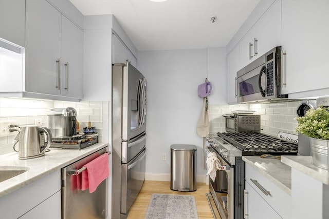 kitchen featuring light stone counters, tasteful backsplash, light wood-style floors, baseboards, and appliances with stainless steel finishes