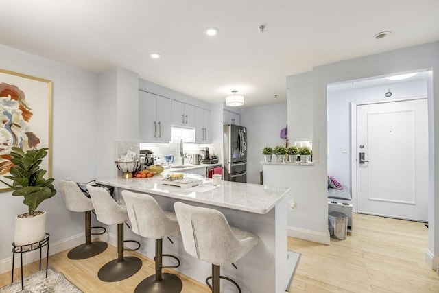 kitchen featuring a peninsula, light wood finished floors, a kitchen bar, and stainless steel refrigerator with ice dispenser