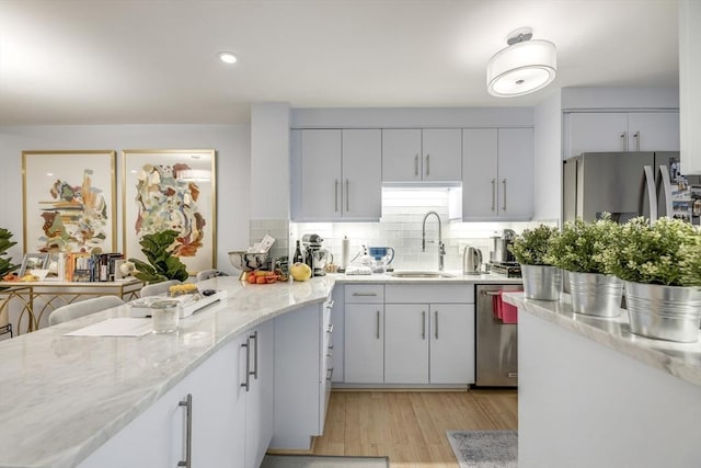 kitchen with light wood finished floors, stainless steel appliances, a sink, light stone countertops, and tasteful backsplash