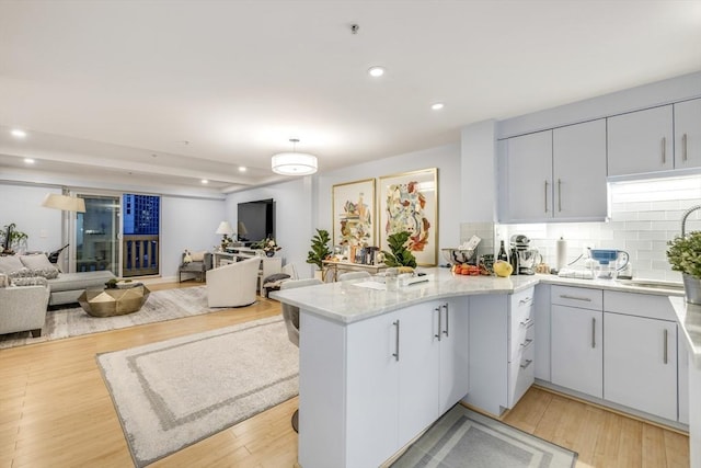 kitchen featuring a peninsula, light wood-style floors, tasteful backsplash, and open floor plan