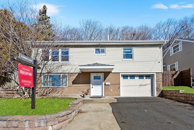 traditional-style home with a garage, aphalt driveway, fence, and stucco siding