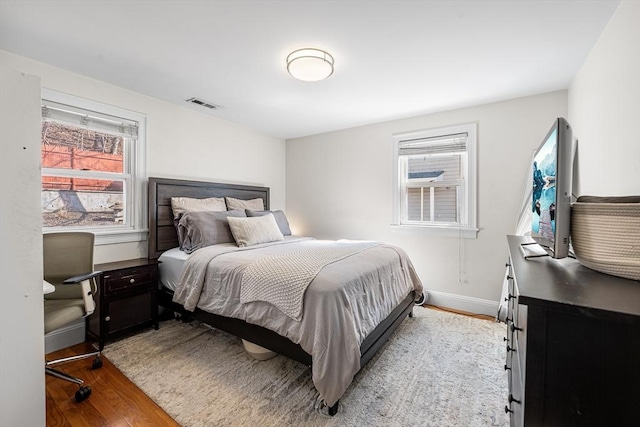 bedroom with baseboards, multiple windows, visible vents, and wood finished floors