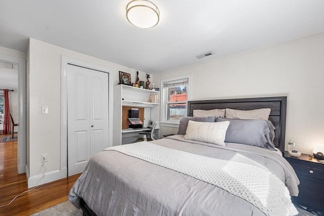 bedroom featuring baseboards, visible vents, a closet, and wood finished floors