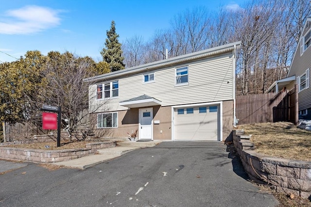 view of front of house with an attached garage, driveway, fence, and stucco siding