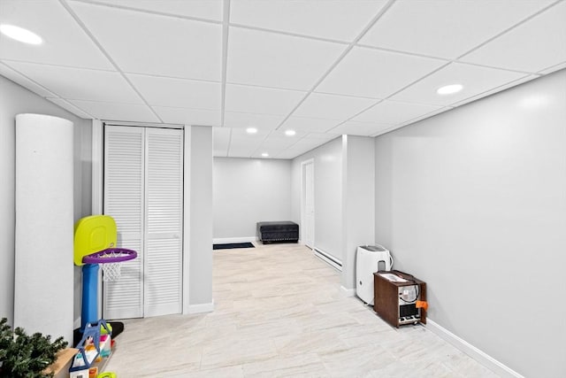 basement featuring a paneled ceiling and a baseboard heating unit