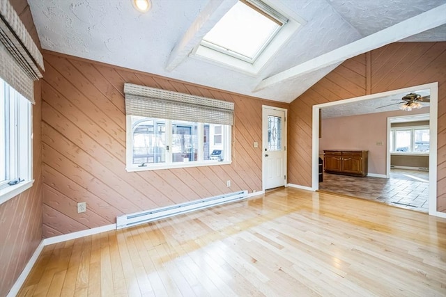 unfurnished living room with ceiling fan, a baseboard heating unit, light wood-type flooring, and vaulted ceiling with skylight