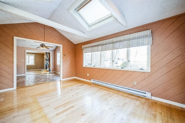 unfurnished room with wooden walls, a textured ceiling, hardwood / wood-style floors, a baseboard heating unit, and vaulted ceiling with skylight