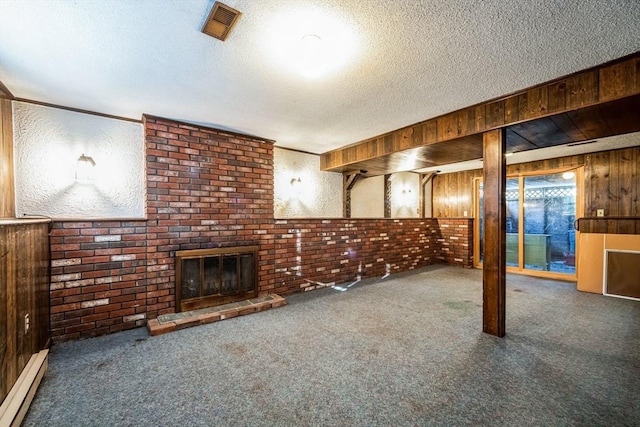 basement with baseboard heating, a textured ceiling, wood walls, and a brick fireplace