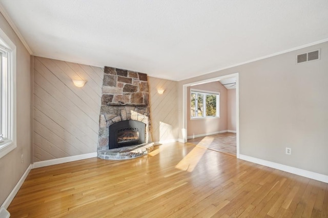 unfurnished living room featuring light wood-type flooring, wooden walls, and a stone fireplace