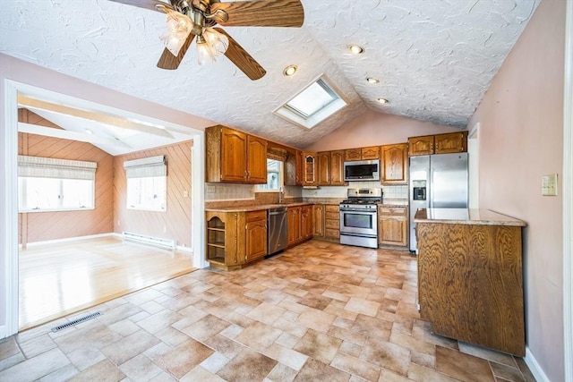 kitchen with stainless steel appliances, lofted ceiling with skylight, ceiling fan, a baseboard radiator, and sink