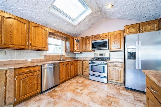 kitchen featuring appliances with stainless steel finishes, vaulted ceiling with skylight, tasteful backsplash, and sink