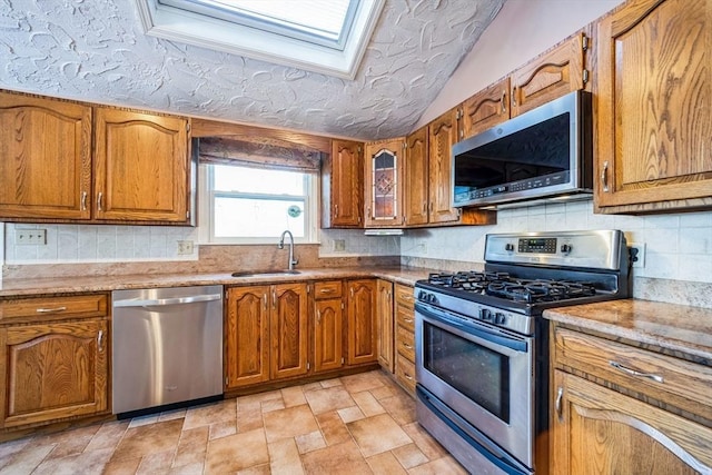 kitchen featuring stainless steel appliances, light stone countertops, a textured ceiling, vaulted ceiling with skylight, and sink