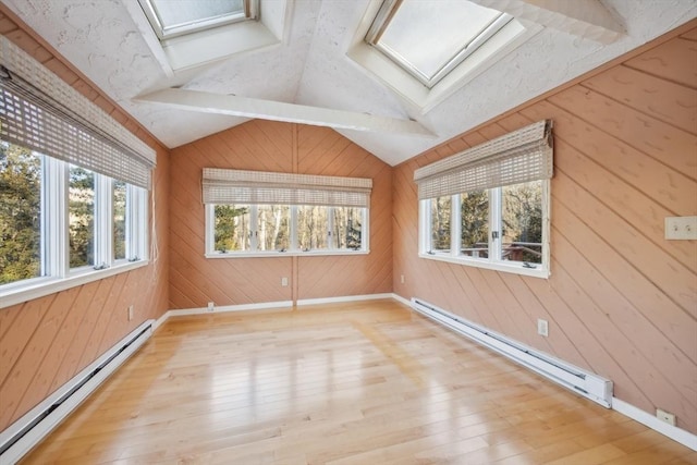 unfurnished room featuring light hardwood / wood-style flooring, vaulted ceiling with skylight, wood walls, and a baseboard heating unit