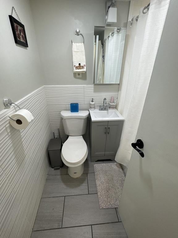 bathroom featuring tile patterned floors, vanity, toilet, and tile walls