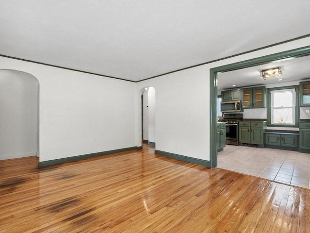 unfurnished living room with light wood-type flooring, arched walkways, and baseboards