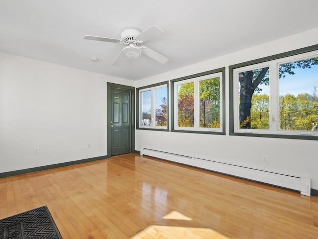 empty room featuring plenty of natural light, a baseboard radiator, baseboards, and hardwood / wood-style floors
