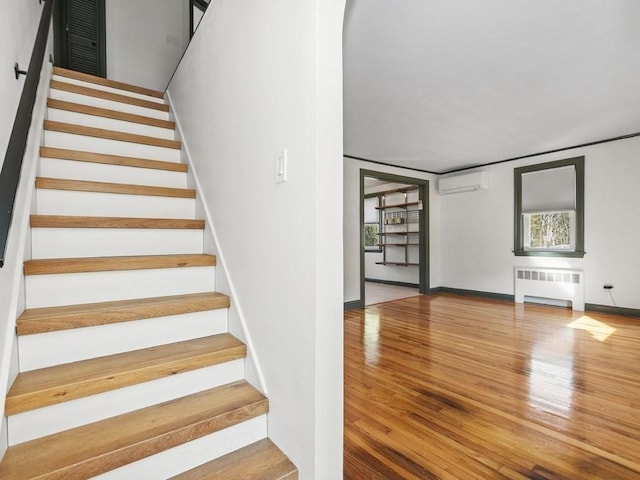 staircase featuring arched walkways, wood finished floors, baseboards, an AC wall unit, and radiator heating unit