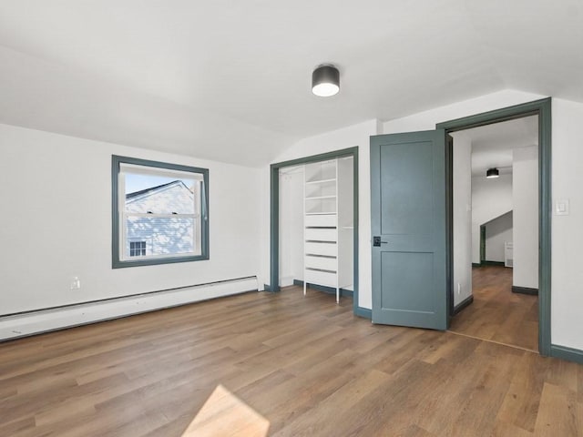 unfurnished bedroom with light wood-style floors, a closet, a baseboard heating unit, and lofted ceiling