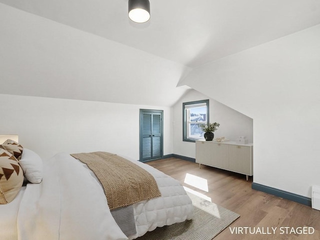 bedroom with baseboards, light wood finished floors, and lofted ceiling