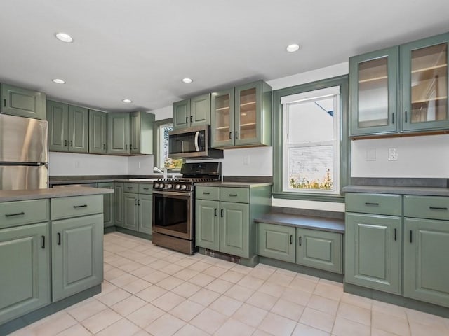 kitchen featuring green cabinetry, appliances with stainless steel finishes, a sink, recessed lighting, and glass insert cabinets