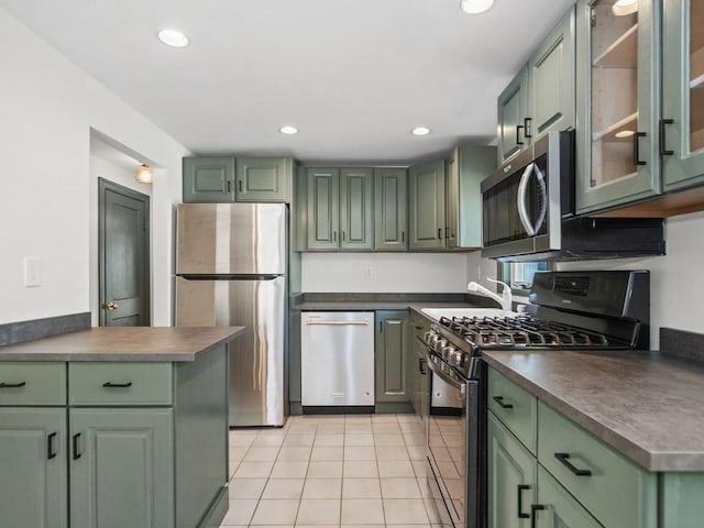 kitchen with green cabinetry, light tile patterned floors, dark countertops, and stainless steel appliances