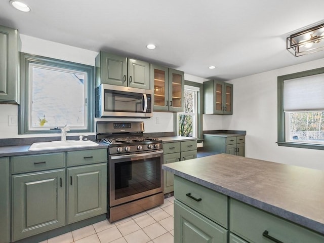 kitchen with appliances with stainless steel finishes, a sink, light tile patterned floors, glass insert cabinets, and green cabinets