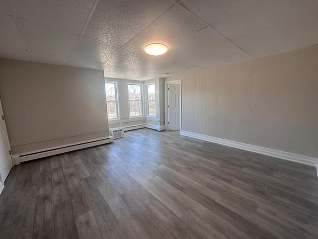 empty room featuring a paneled ceiling, baseboard heating, baseboards, and dark wood-style flooring