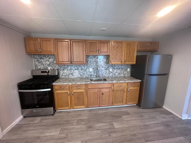 kitchen with light wood-type flooring, baseboards, stainless steel appliances, and a sink