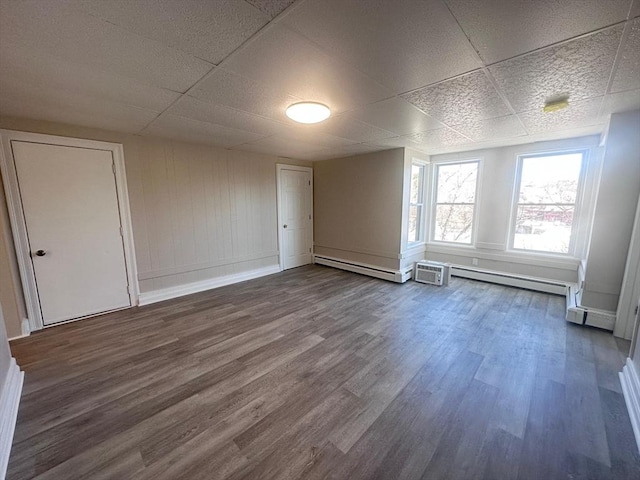 empty room with dark wood-type flooring, a drop ceiling, and baseboards