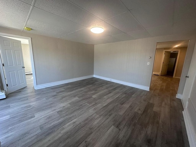 spare room featuring dark wood finished floors, a drop ceiling, wood walls, a baseboard heating unit, and baseboards
