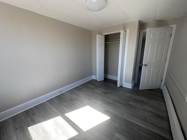 unfurnished bedroom with a baseboard radiator, baseboards, wood finished floors, and a paneled ceiling