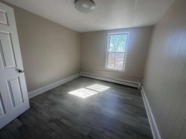 empty room featuring a baseboard heating unit, baseboards, dark wood-type flooring, and wooden walls