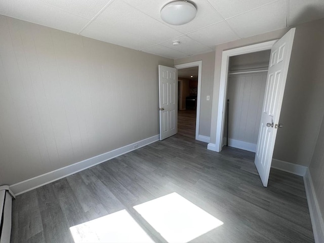 unfurnished bedroom with a paneled ceiling, wood finished floors, baseboards, and a closet