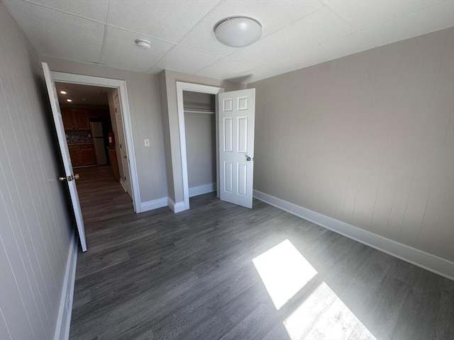 unfurnished bedroom featuring baseboards, a paneled ceiling, wood finished floors, and a closet