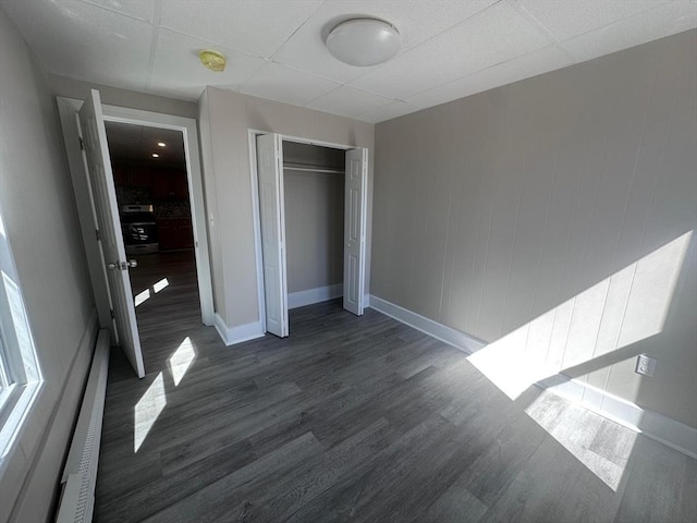 unfurnished bedroom with a paneled ceiling, baseboards, a closet, and dark wood-style flooring