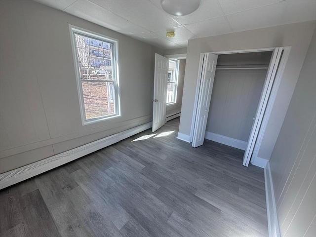 unfurnished bedroom featuring wood finished floors, baseboards, a closet, and baseboard heating