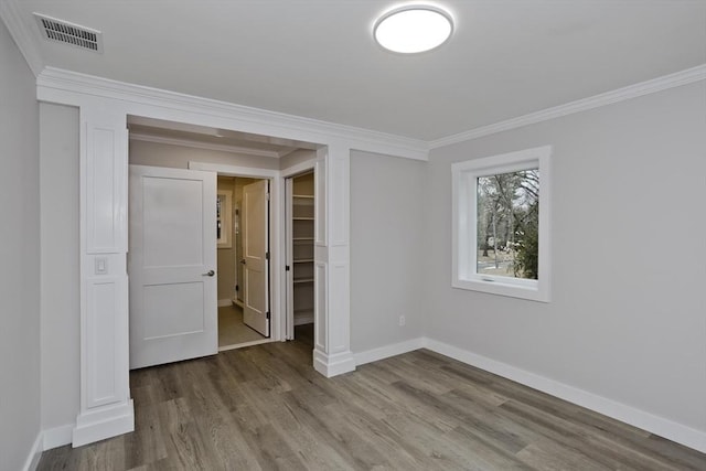 unfurnished bedroom featuring visible vents, crown molding, baseboards, and wood finished floors