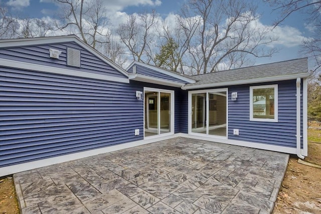 back of property with a shingled roof and a patio