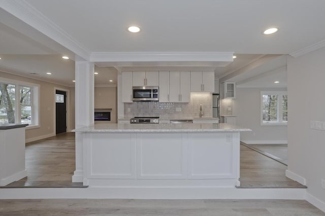 kitchen with a healthy amount of sunlight, appliances with stainless steel finishes, decorative backsplash, light wood finished floors, and crown molding