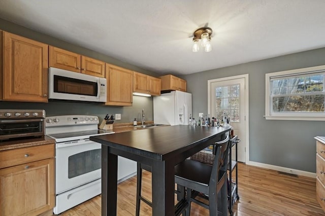 kitchen featuring visible vents, light wood-type flooring, a sink, white appliances, and baseboards