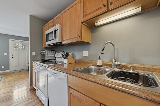 kitchen with baseboards, light wood-style floors, brown cabinetry, white appliances, and a sink