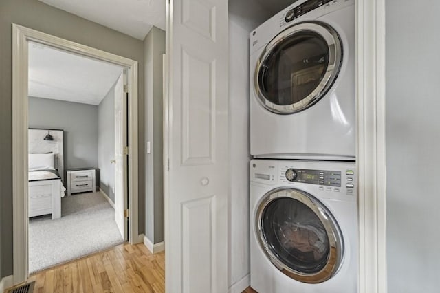 washroom with baseboards, visible vents, stacked washing maching and dryer, laundry area, and light wood-style floors