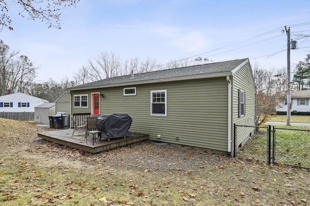 rear view of property with fence, a wooden deck, an outdoor structure, a storage unit, and a gate