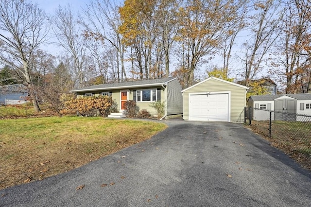 view of front facade featuring fence, an outdoor structure, a front lawn, a garage, and aphalt driveway