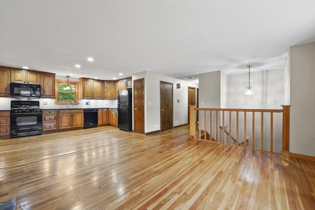 kitchen with black appliances, a sink, light wood-style flooring, brown cabinetry, and decorative light fixtures